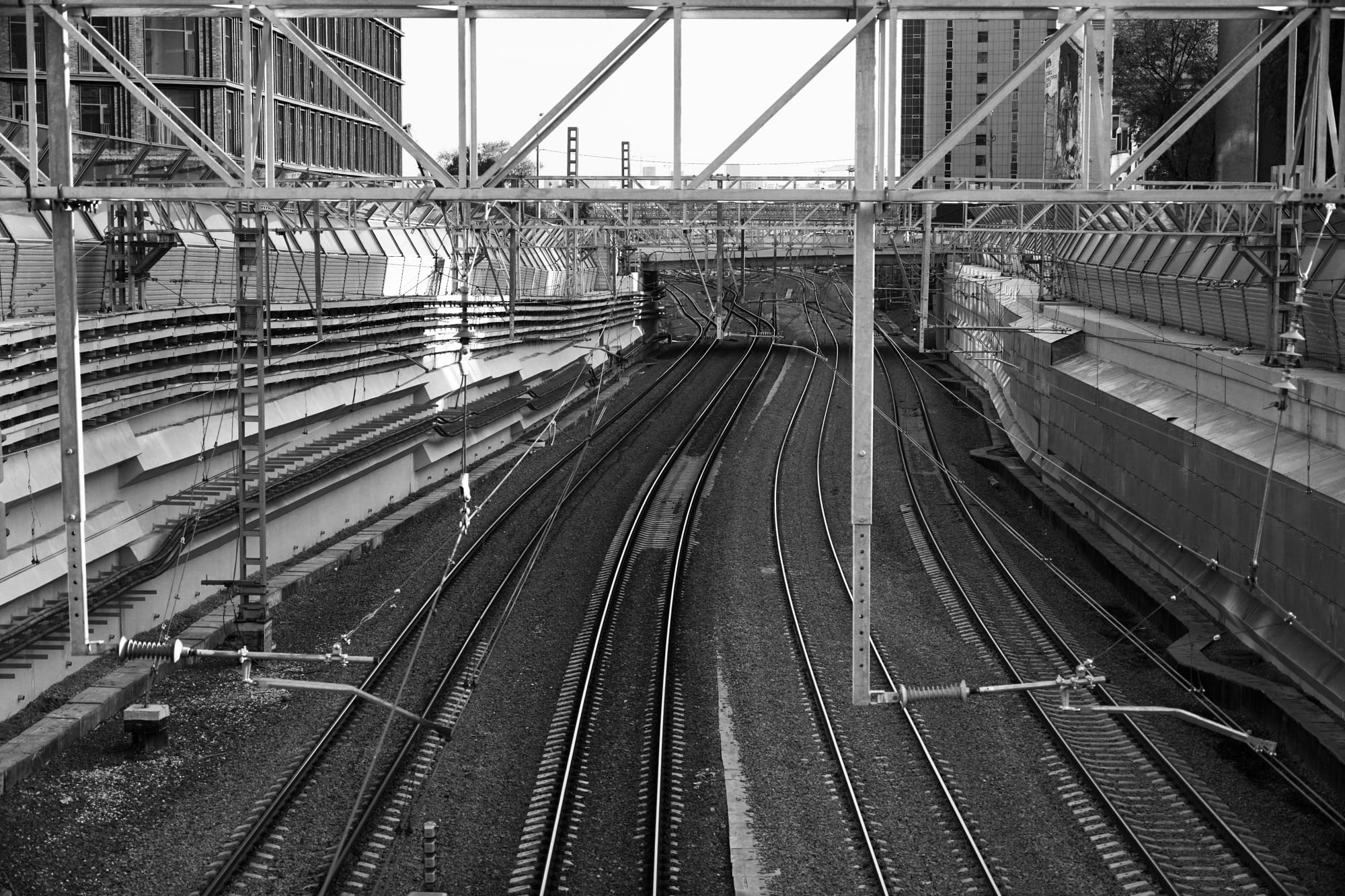 Monochrome image of empty urban railway tracks surrounded by structures.